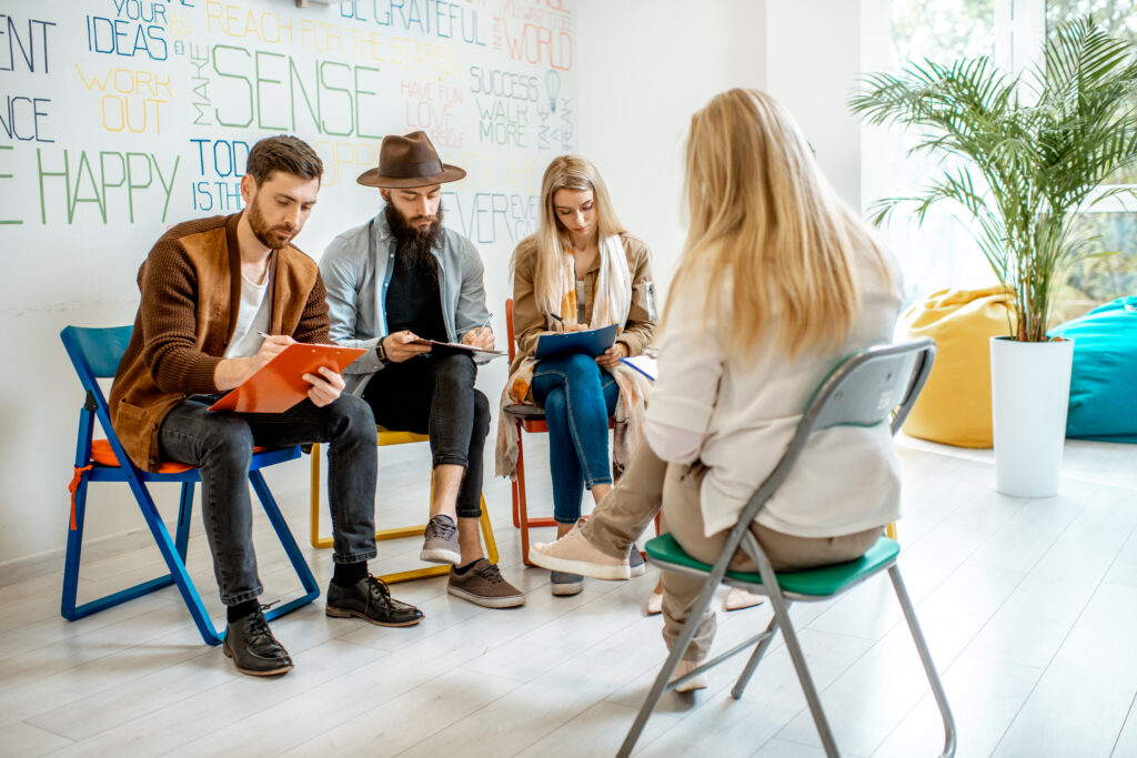 Group of young people sitting together during the psychological therapy with psychologist solving some mental problems in the office